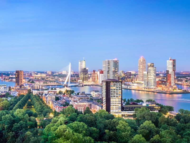 An aerial view of the city of Rotterdam with the Maas river, the Erasmus bridge, high buildings and greenery.